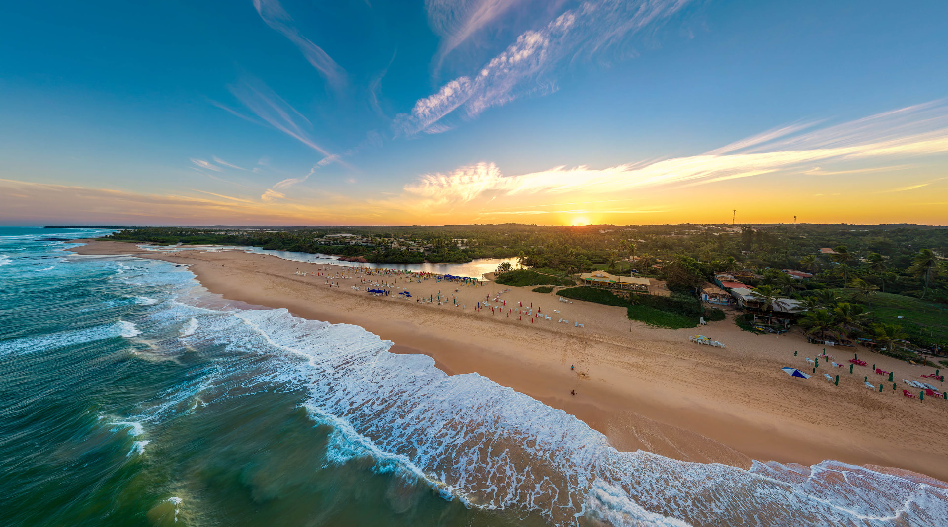 Vista aérea da praia de Imbassaí ao pôr do sol, com o encontro do rio e do mar