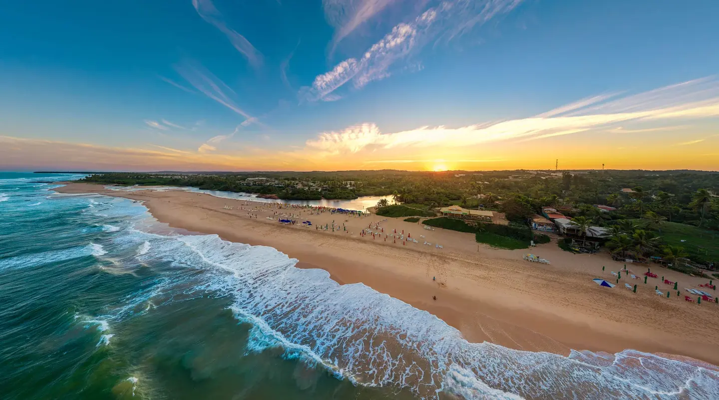 Vista aérea da praia de Imbassaí ao pôr do sol, com o encontro do rio e do mar